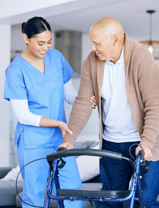 Comprehensive Overnight Care Services in Edmonton-image A nurse in blue scrubs gently assists an elderly man using a walker. The scene conveys warmth and care in a home setting, highlighting supportive healthcare.