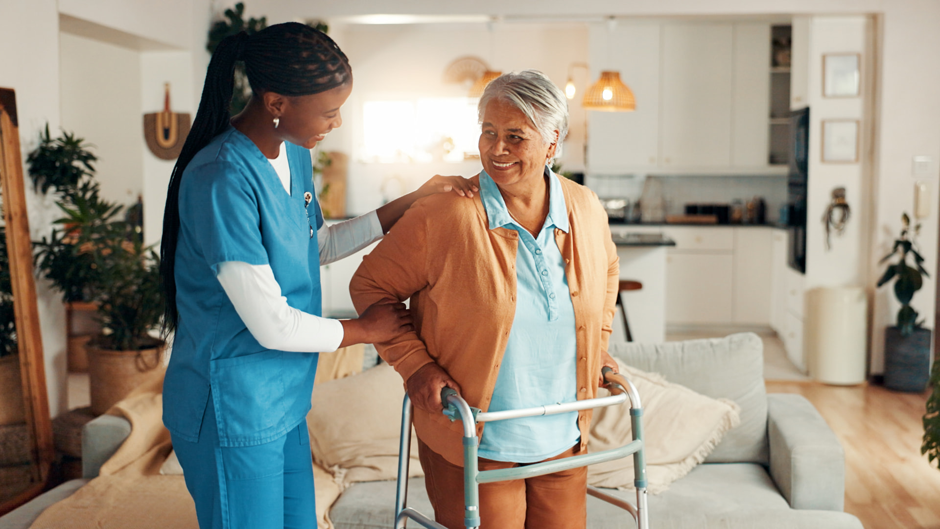 Caregiver supporting an older woman using a walker at home.