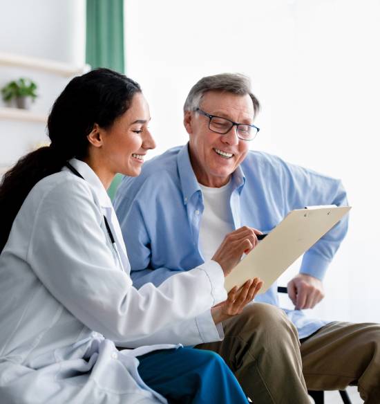 Our Dedicated Overnight Caregivers in Edmonton-image A smiling doctor explains medical notes on a clipboard to an elderly patient. Both appear content and engaged in a bright, friendly office setting.