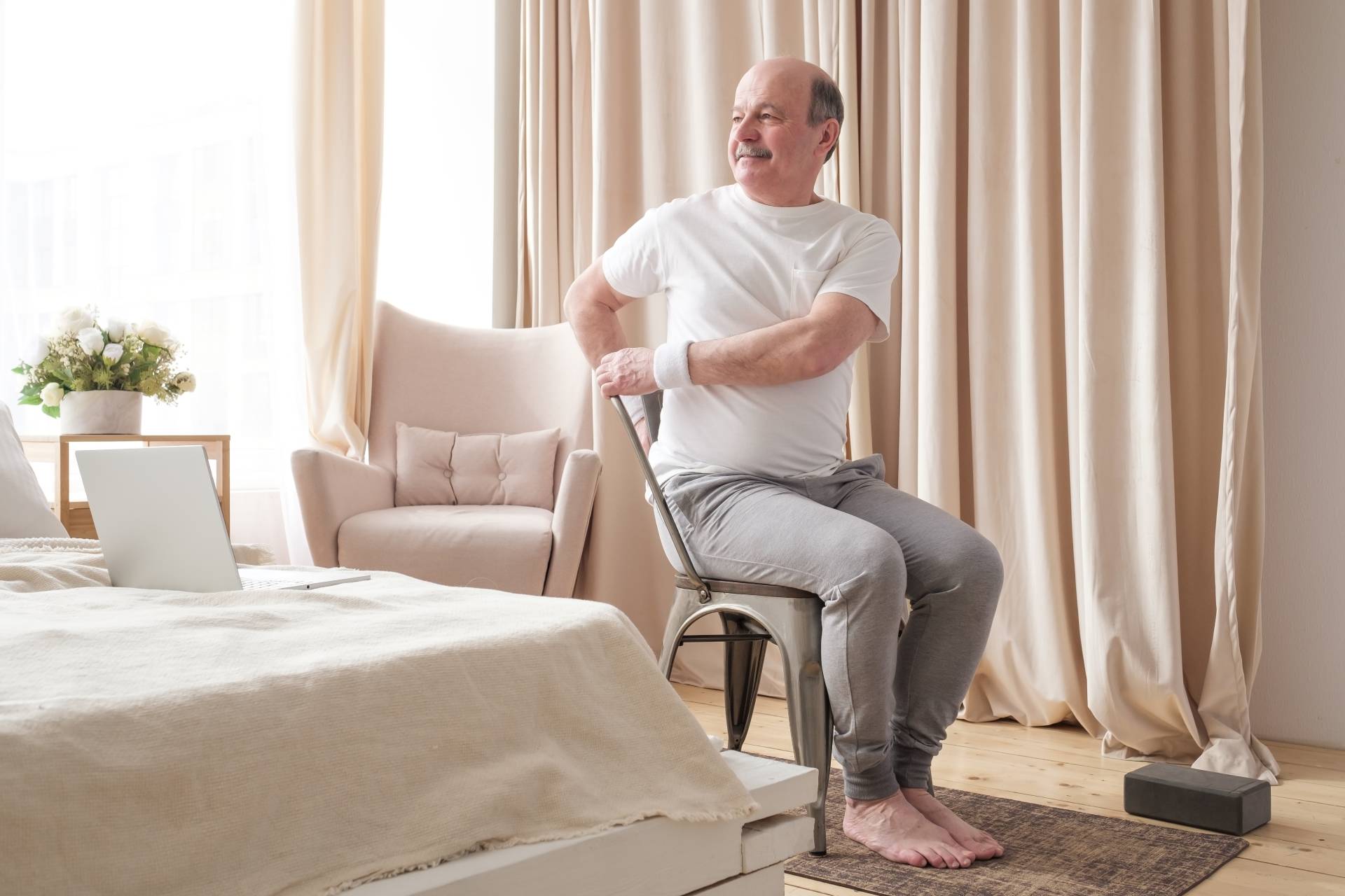 Senior man doing a seated abdominal twist in his bedroom.