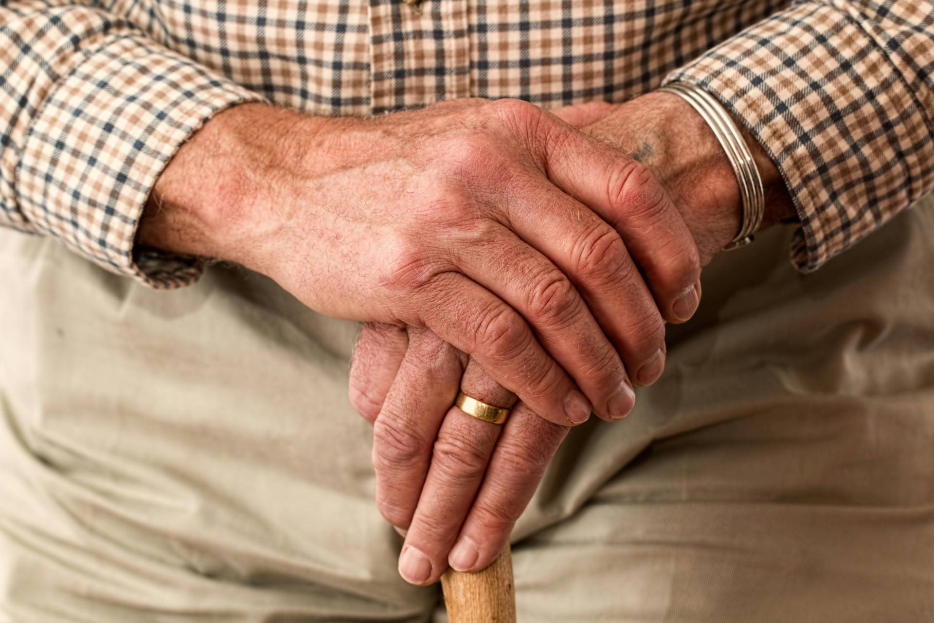 A close-up of an elderly person's hands resting on a wooden cane.