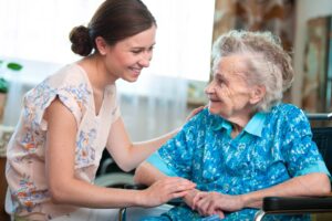 A caregiver sitting with an elderly woman in a wheelchair.