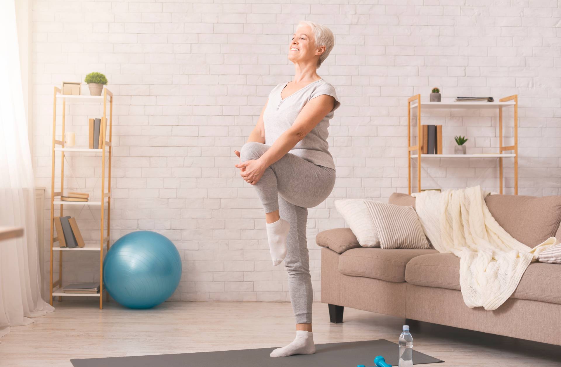 Old woman doing a single-leg stance in her living room.