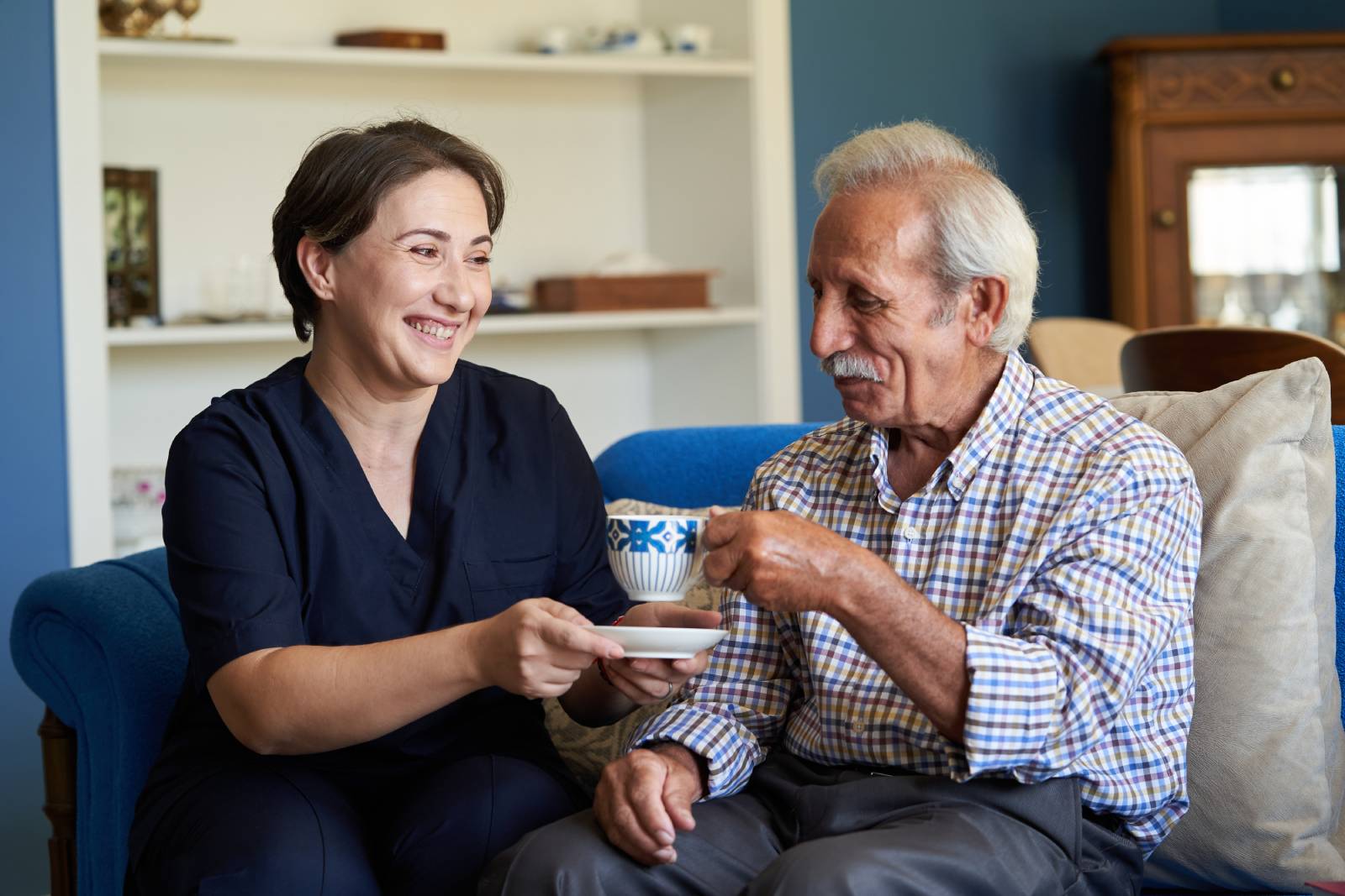 A caregiver sitting on a couch drinking tea with a senior.