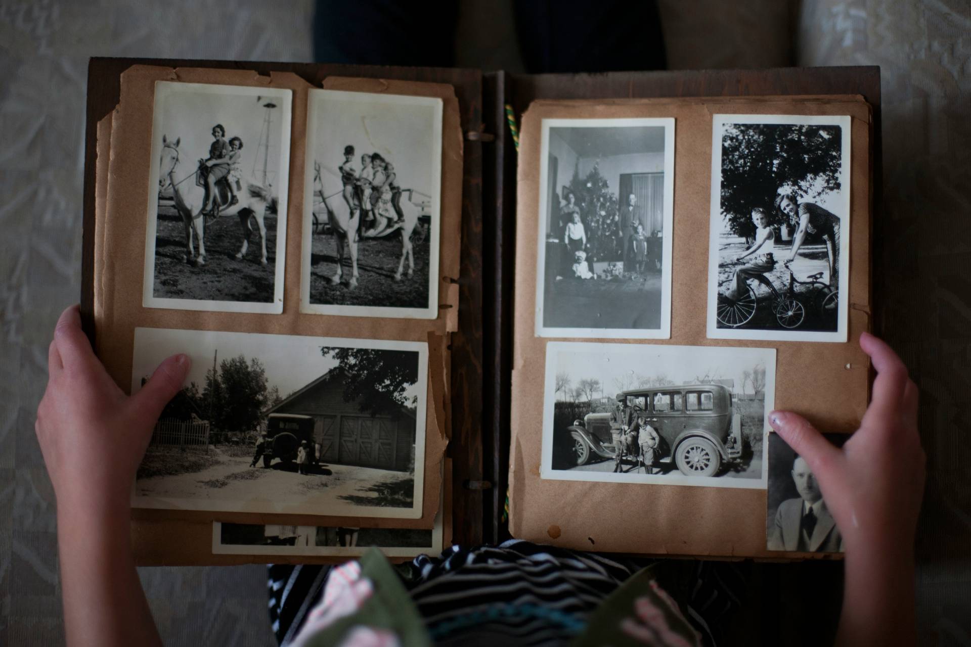 A person holding an open photo album with old black-and-white photographs.