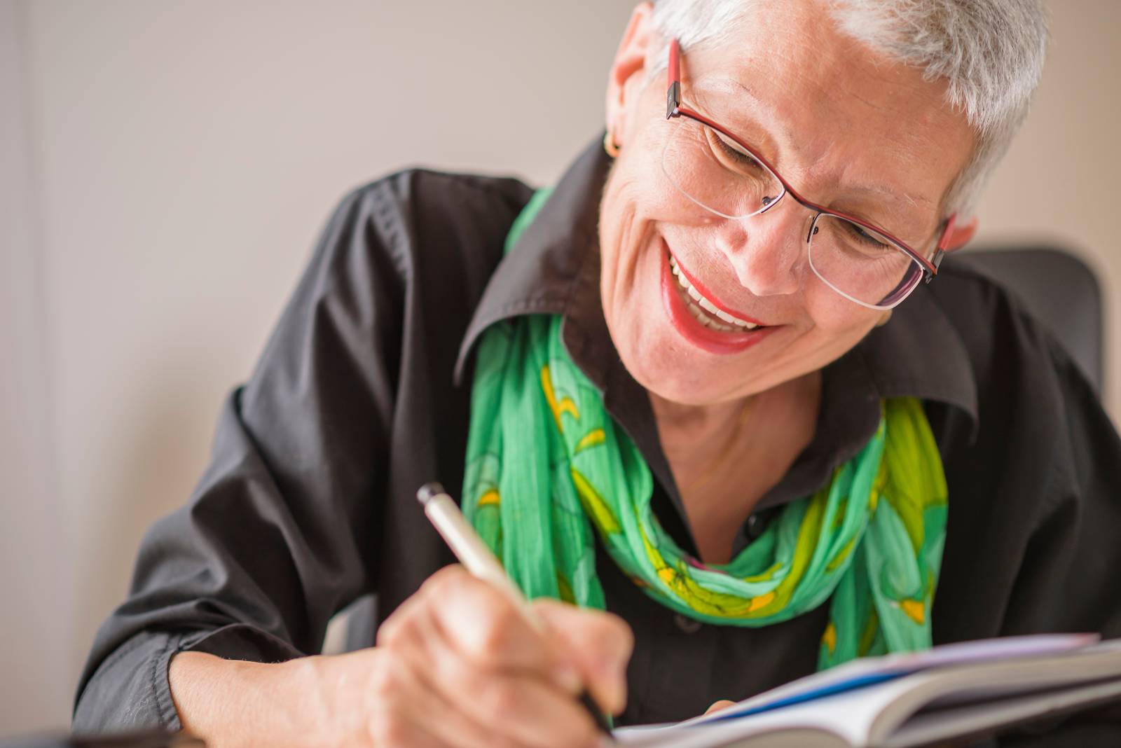 Elderly woman smiling while writing a note.