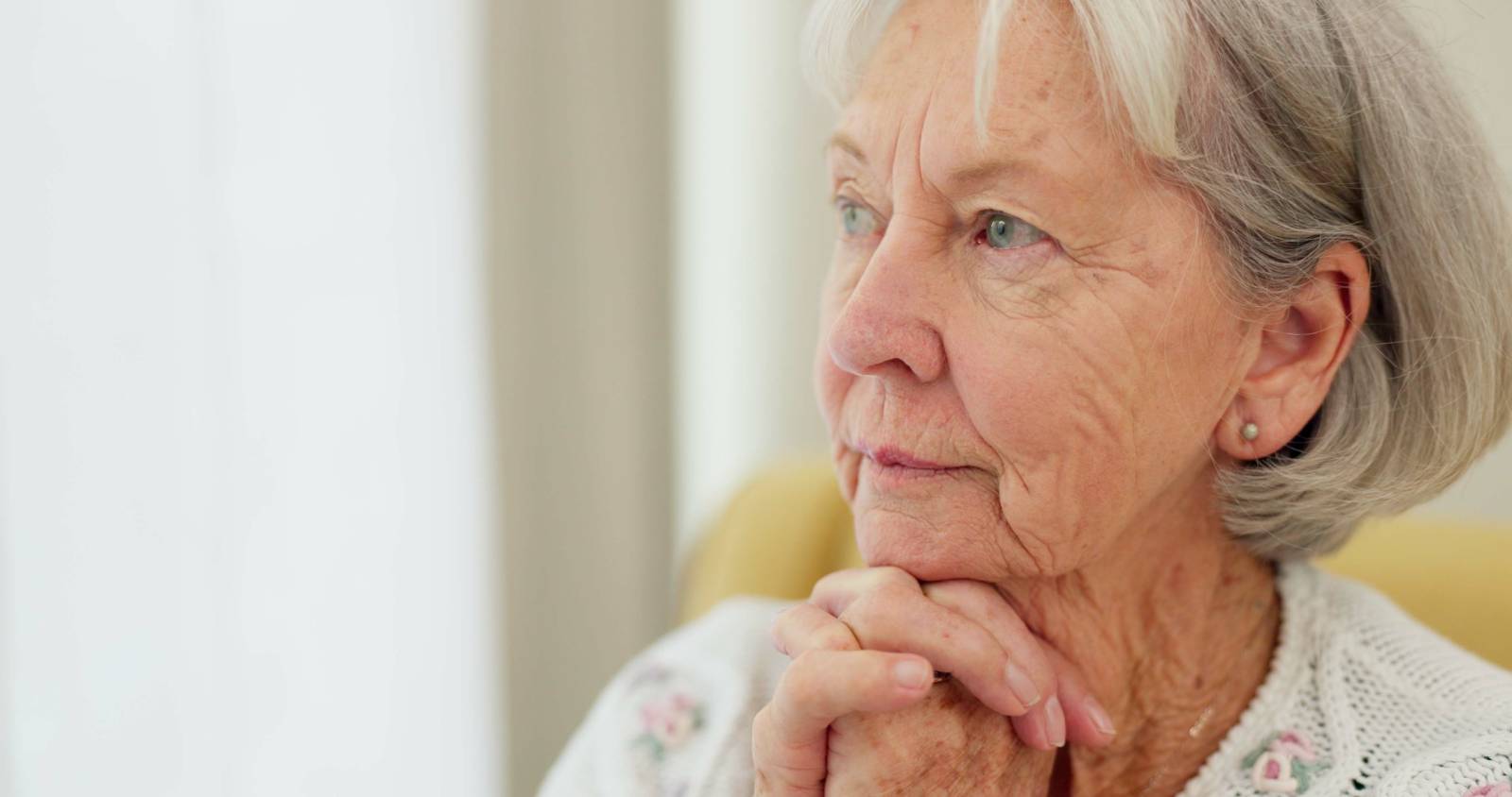 An elderly woman with grey hair is gazing thoughtfully to the side.